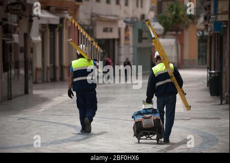 Construction workers walking on an almost deserted street during the covid-19 crisis.Following the confinement decreed by the Spanish government and will extended until 10th May, people are confinement in their homes causing an exceptional situation of unusual urban scenes such as empty streets. Stock Photo