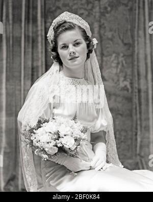 1930s PORTRAIT OF SEATED BRIDE WEARING GOWN VEIL HOLDING BOUQUET LOOKING AT CAMERA - b14929 HAR001 HARS COPY SPACE FRIENDSHIP HALF-LENGTH LADIES MARRIAGE PERSONS INSPIRATION SATIN VEIL CEREMONY B&W BRIDAL EYE CONTACT BRUNETTE HAPPINESS BRIDES CUSTOM EXCITEMENT TRADITION NUPTIAL NUPTIALS OCCASION MARRYING PRIDE WHITE  CONCEPTUAL HEADPIECE LILY OF THE VALLEY RITE OF PASSAGE STYLISH WED MARRY MATRIMONY YOUNG ADULT WOMAN BLACK AND WHITE CAUCASIAN ETHNICITY HAR001 OLD FASHIONED Stock Photo