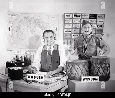 1950s HAM RADIO HOBBY COMMUNICATIONS FATHER IN HEADPHONES AND SON A BOY SCOUT PLAYING TOM TOM DRUMS AMID SHORT WAVE RADIO GEAR - b3776 LEF001 HARS COMMUNICATION TEAMWORK RELAXING SONS FAMILIES LIFESTYLE SCOUT COPY SPACE HALF-LENGTH DRUMS PERSONS DOING SCOUTS MALES HAM SYMBOLS CONFIDENCE FATHERS B&W EYE CONTACT SKILL ACTIVITY AMUSEMENT HAPPINESS CHEERFUL BROADCASTING HOBBY INTEREST AND NETWORKING DADS HOBBIES KNOWLEDGE PASTIME PLEASURE A IN OPPORTUNITY HEADPHONES BOY SCOUT CONCEPT CONNECTION THRIFTY TRANSMISSION CONCEPTUAL COURTEOUS FRIENDLY HELPFUL KIND REVERENT TRUSTWORTHY SYMBOLIC TRANSMIT Stock Photo