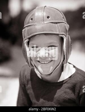 1930s SMILING SQUINTING BOY WEARING LEATHER FOOTBALL HELMET LOOKING AT CAMERA - b63 HAR001 HARS ATHLETE PLEASED JOY LIFESTYLE SATISFACTION RURAL HEALTHINESS COPY SPACE MALES RISK ATHLETIC CONFIDENCE EXPRESSIONS B&W EYE CONTACT GOALS ACTIVITY DREAMS HAPPINESS PHYSICAL HEAD AND SHOULDERS CHEERFUL STRENGTH EXCITEMENT RECREATION SQUINTING PRIDE SMILES FLEXIBILITY JOYFUL MUSCLES FOOTBALLS GROWTH JUVENILES AMERICAN FOOTBALL BLACK AND WHITE CAUCASIAN ETHNICITY HAR001 OLD FASHIONED Stock Photo