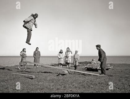 1940s 1950s ALASKAN ESKIMO CHILDREN AND TEENS PLAYING A GAME OF JUMPBOARD A KIND OF SEESAW GAME ARCTIC KOTZEBUE ALASKA USA - c2676 BAU001 HARS TEAMWORK LEAPING JOY LIFESTYLE FEMALES ESKIMO RURAL UNITED STATES COPY SPACE FRIENDSHIP FULL-LENGTH PERSONS SEESAW INDIANS UNITED STATES OF AMERICA MALES TEENAGE GIRL TEENAGE BOY B&W NORTH AMERICA NORTH AMERICAN ALASKA HUMOROUS LEAP AND RECREATION COMICAL INUIT COMEDY KIND TEENAGED KOTZEBUE NATIVE AMERICAN ARCTIC COOPERATION GROWTH JUVENILES NATIVE AMERICANS PRE-TEEN ALASKAN BLACK AND WHITE INDIGENOUS OLD FASHIONED PARKAS Stock Photo