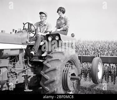 1970s YOUNG SMILING FARM COUPLE MAN AND WOMAN RIDING ON A TRACTOR PULLING CULTIVATOR BY CORNFIELD HUSBAND DRIVING WIFE RIDING - f13312 HAR001 HARS OLD TIME BUSY FUTURE NOSTALGIA OLD FASHION 1 STEERING YOUNG ADULT BALANCE SAFETY TEAMWORK PLEASED FAMILIES JOY LIFESTYLE SATISFACTION FEMALES TRACTOR MARRIED JOBS RURAL SPOUSE HUSBANDS HEALTHINESS HOME LIFE UNITED STATES COPY SPACE FULL-LENGTH HALF-LENGTH LADIES PERSONS UNITED STATES OF AMERICA FARMING MALES RISK SERENITY SPIRITUALITY CONFIDENCE AGRICULTURE B&W PARTNER NORTH AMERICA FREEDOM NORTH AMERICAN SUCCESS SKILL DREAMS OCCUPATION HAPPINESS Stock Photo