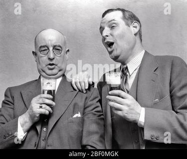 1930s TWO DRUNKEN BUSINESSMEN CELEBRATING SINGING AND DRINKING BEER - f453 HAR001 HARS SATISFACTION CELEBRATION STUDIO SHOT COPY SPACE FRIENDSHIP HALF-LENGTH PERSONS MALES SENIOR MAN SENIOR ADULT EXPRESSIONS B&W BIZARRE SUIT AND TIE CELEBRATING HUMOROUS HAPPINESS WEIRD BEVERAGE AND GROTESQUE FLUID SONG VOCAL ZANY COMICAL UNCONVENTIONAL ENTERTAINER CONNECTION DRUNKEN INTOXICATED VOCALIZE CONCEPTUAL VOCALS COMEDY CONSUME CONSUMING FRIENDLY HYDRATION INEBRIATED SONGS WACKY IDIOSYNCRATIC AMUSING BREWSKI COOPERATION ECCENTRIC MID-ADULT MID-ADULT MAN REFRESHING TOGETHERNESS BEVERAGES BLACK AND WHITE Stock Photo