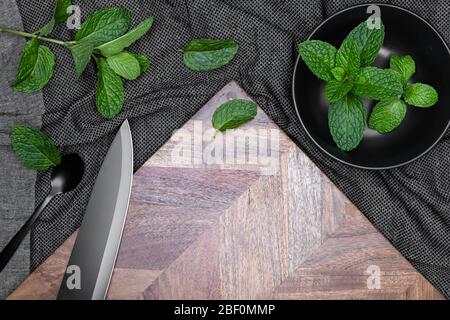 Black bowl, Knife and spoon with fresh herbs - Mints on dark background and wooden chopping board.  For copy space. Stock Photo