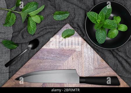Black bowl, Knife and spoon with fresh herbs - Mints on dark background and wooden chopping board.  For copy space. Stock Photo