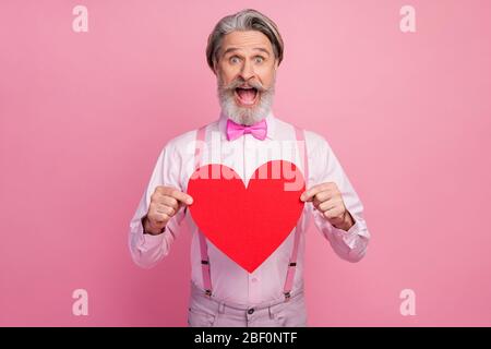Portrait of his he nice attractive imposing ecstatic overjoyed cheerful cheery grey-haired man holding in hands big large red heart isolated over pink Stock Photo