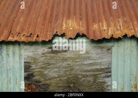 rusty corrugated-iron roof and wall of a boarded-up old cabin Stock Photo
