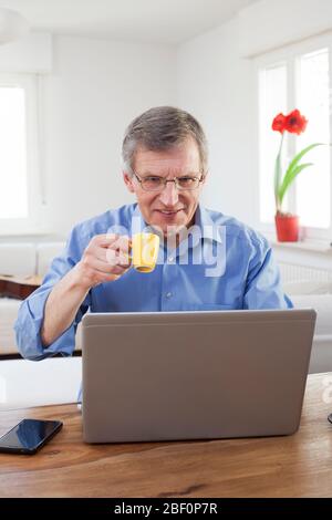 Senior or mature businessman drinking espresso in front of a computer in his home office - focus on the face Stock Photo