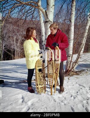 1960s YOUNG COUPLE MAN AND WOMAN STANDING TALKING IN SNOWY WOODS HOLDING TRADITIONAL BENT HARDWOOD AND WOVEN RAWHIDE SNOWSHOES  - kw2780 HAR001 HARS COMMUNICATION HEALTHY SAFETY TEAMWORK ATHLETE JOY LIFESTYLE FEMALES MARRIED RURAL SPOUSE HUSBANDS ATHLETICS COPY SPACE FRIENDSHIP FULL-LENGTH LADIES PHYSICAL FITNESS PERSONS INSPIRATION TRADITIONAL MALES ATHLETIC CONFIDENCE SNOWY PARTNER WINTERTIME FREEDOM ACTIVITY HAPPINESS PHYSICAL WELLNESS ADVENTURE LEISURE STRENGTH AND CHOICE RECREATION IN CONNECTION ATHLETES BENT FLEXIBILITY HARDWOOD MUSCLES RAWHIDE STYLISH FOOTWEAR WINTERY RELAXATION Stock Photo