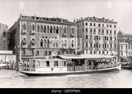 1920s FERRY BOAT DELIVERING PEOPLE GUESTS TO LUXURY HOTEL ROYAL DANIELI FORMERLY LATE 14TH CENTURY PALAZZO DANDOLO VENICE ITALY - q25 HAR001 HARS TO GUESTS REAL ESTATE ROYAL STRUCTURES 14TH FERRY EDIFICE FORMERLY 14TH CENTURY BUILT CANAL HOTELS LAVISH BLACK AND WHITE GRAND CANAL HAR001 OLD FASHIONED PALAZZO Stock Photo