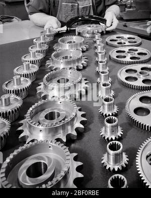 1970s MALE HANDS PERFORMING QUALITY CHECK ON 3 ASSEMBLED GEAR PIECES TAKEN FROM THE ROWS OF SPINDLES GEARS IN FRONT OF HIM  - s17875 HAR001 HARS GEARS HIGH ANGLE LABOR OF ON THE EMPLOYMENT OCCUPATIONS QUALITY ROWS CONCEPT CONCEPTUAL ASSEMBLED IN FRONT OF EMPLOYEE SYMBOLIC CONCEPTS HIM MACHINING PRECISION QUALITY CONTROL SPINDLES TOOTHED BLACK AND WHITE CAUCASIAN ETHNICITY HANDS ONLY HAR001 LABORING OLD FASHIONED PARTS REPRESENTATION Stock Photo