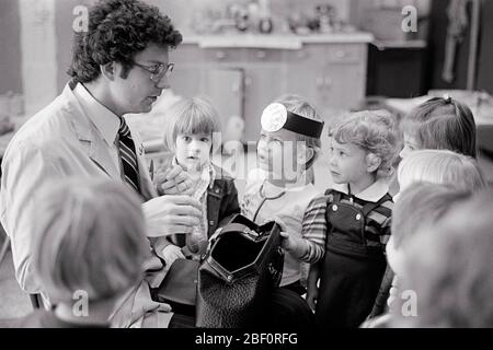 1970s MEDICAL DOCTOR TALKING TO FIRST GRADE CLASS ON HIS WORK AND PROFESSION IN MEDICINE - s21644 HAR001 HARS 1 JUVENILE ELEMENTARY COMMUNICATION LIFESTYLE FEMALES JOBS HEALTHINESS ILLNESS COPY SPACE HALF-LENGTH PHYSICAL FITNESS PERSONS CARING MALES PROFESSION B&W HEALTHCARE SCHOOLS SKILL GRADE OCCUPATION SKILLS WELLNESS PREVENTION PROVIDER PROVIDERS DISCOVERY HIS PRACTITIONERS HEALING AND DIAGNOSIS CHOICE EXCITEMENT KNOWLEDGE PHYSICIANS PRIDE HEALTH CARE AUTHORITY FACIAL HAIR IMPAIRMENT OCCUPATIONS PRIMARY TREATMENT CONNECTION HEALER PHYSICIAN PRACTITIONER GRADE SCHOOL GROWTH JUVENILES Stock Photo