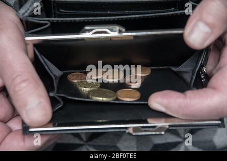 A man opens and holds an empty wallet with coins. money ran out due to quarantine. Stock Photo