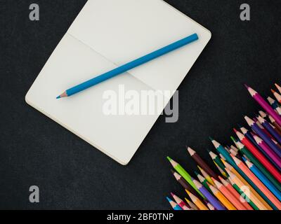 Set of colored pencils and notebook on slate background. top view Stock Photo