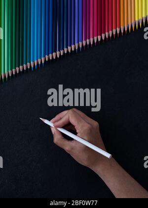 olored pencils in a row, caucasian female hand writing on slate background. top view Stock Photo