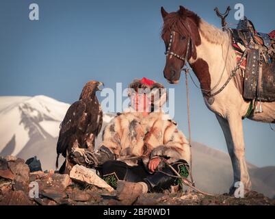 Mongolian eagle hunter, Kazakh with trained eagle in front of mountains, Bajan-Oelgii province, Mongolia Stock Photo