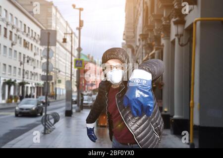A man in a protective mask and gloves with the inscription COVID-19 against the backdrop of an urban environment. Coronavirus infection protection Stock Photo