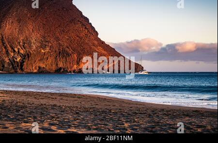 Sunset at La Tejita beach with a yacht moored near the iconic 'Red Hill' (La Montaña Roja) in the South of Tenerife, Canary Islands, Spain. Stock Photo