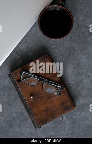 Brown leather notebook, pen, laptop and glasses on gray background. Stock Photo