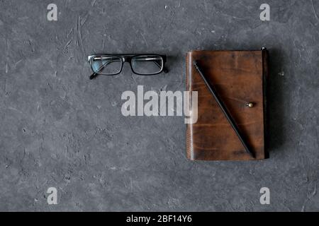 Brown craft leather notebook, pen and glasses on gray background. Stock Photo