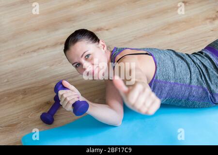 Woman in sportswear on the floor with dumbbells at home in the living room. Workout online concept. Stock Photo