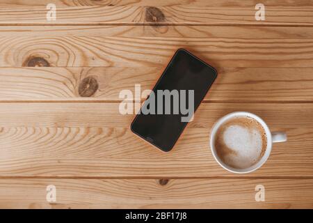 Smartphone and a cup of coffee on a wooden desk. Light wood background. Stock Photo