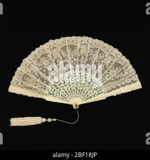 Pleated fan. Pleated fan. Leaf ofwhite cotton bobbin-made Valenciennes lace in floral design, backed with silk net. Sticks of pierced and carved ivory in floral design. Guards with figures of birds, cupids and insects. Metal loop at the rivet. Attached tassel. Stock Photo