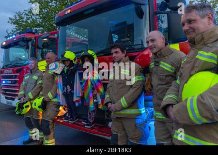 Southend-on-Sea, UK. 16th Apr, 2020. Firefighters from Essex Fire Brigade stand with children in rainbow capes outside Southend Hospital during a Clap for Carers tribute amid the COVID-19 pandemic. Blue emergency lights illuminate the scene, symbolising solidarity and public appreciation for NHS staff. Penelope Barritt/Alamy Live News Stock Photo