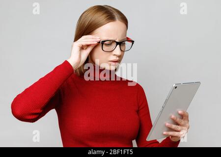 Astonished and surprised stylish business woman in red turtleneck using tablet computer, reads something important about coronavirus and economics, ho Stock Photo