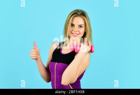 be successful. girl use barbell blue background. Slim girl doing triceps exercise with dumbbell in the gym. coach dressed in sport clothes. muscular woman in training pumping up muscles of hands. Stock Photo