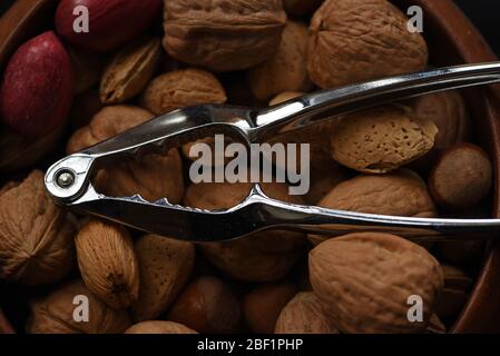 A chrome metal nutcracker lies on top of an assortment of nuts including walnuts and almonds Stock Photo