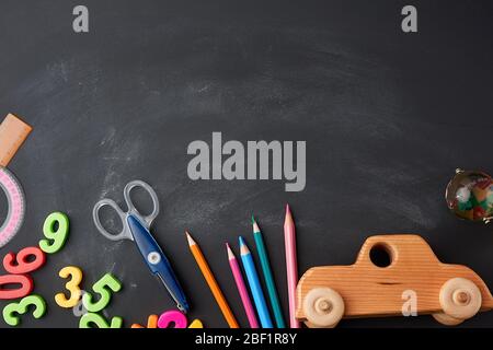 wooden multi-colored pencils, plastic numbers, scissors, wooden toy car on a black background, concept back to school, copy space Stock Photo