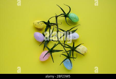 Abstract Easter composition of multicolored eggs, tomato branches and yellow background. Easter background. The concept of spring. Copy the space for Stock Photo