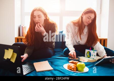 Young women doing homework in a dormitory bed near the window. There are notebooks, food books, a tablet and laptop and documents Stock Photo