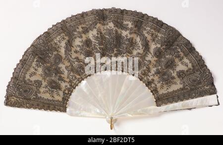 Pleated fan and case. Pleated fan. Leaf of black chantilly lace backed with stiff white georgette crêpe. Mother-of-pearl sticks. White paste jewel rivet heads. Box covered in tan silk marked “Tiffany & Co. Union Square.” Stock Photo