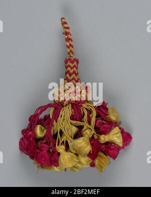 Tassel. Skirt of red and yellow silk threads, twisted and looped and each supporting a small tassel. Collar of cut threads. Head, cylindrical and broadening toward the base, is covered with red and green threads in a chevron pattern. Stock Photo