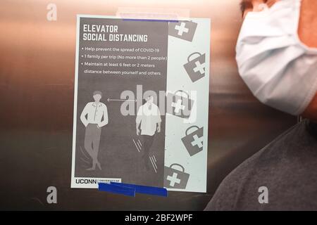Storrs, CT / USA - March 19, 2020: Masked man leans close to a sign posted in elevator detailing proper social distancing procedures Stock Photo