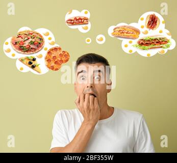 Emotional young man thinking about different fast food on color background Stock Photo