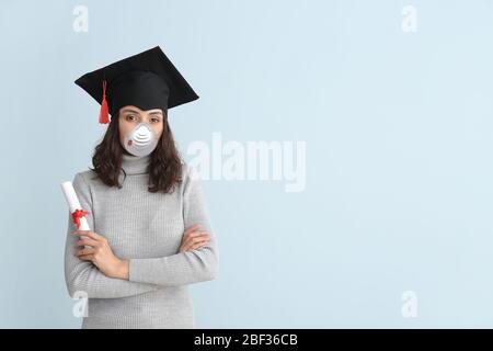 Female graduating student wearing protective mask on light background. Concept of epidemic Stock Photo