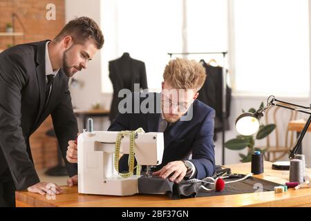 Young male tailor with colleague working on sewing machine in atelier Stock Photo