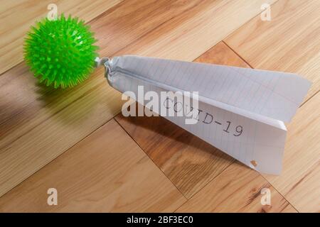 Deadly epidemic coronavirus with paper airplane that reads COVID-19 as metaphor for closed airports Stock Photo