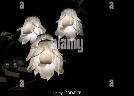 Modern opaque white abstract floral shaped light fixtures hanging from the ceiling with a dark background, high contrast Stock Photo