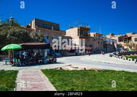 A road winding into the old town with a food stall serving customers in front of a mosque, Kashgar, Xinjiang Province, China Stock Photo