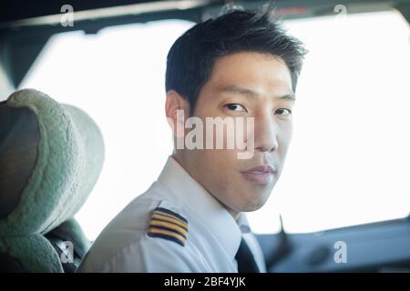 Asian male pilot sitting in the cockpit looking into the camera serioulsy, getting ready to fly the airplane. Stock Photo