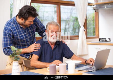 Elder care in home, good mentor healthy smart old man using laptop computer stay at young man. Stock Photo