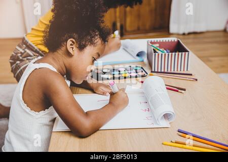 American Black preschool daughter kids doing homework learning education with her sister living together at home. Stock Photo