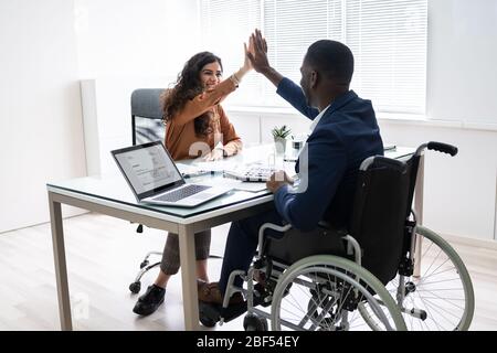 Disabled Businessman Giving High Five To His Smiling Female Partner In Office Stock Photo