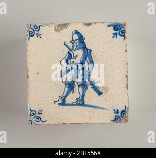 Tile. Square tile, blue on white. Soldier with helmet and breastplate standing with back in three-quarters view. Left arm akimbo, right hand at side, holding gun. Symmetrical scroll ornaments in the corner. Stock Photo