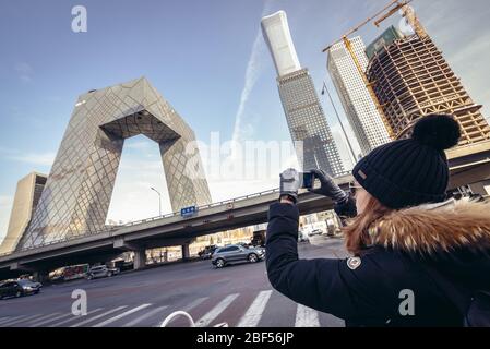 Tourist takes photo of CCTV Headquarters office skyscraper in Beijing central business district, China, view with supertall CITIC Tower Stock Photo