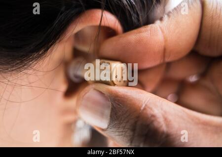 Cropped Image Of Doctor Inserting Hearing Aid In Woman's Ear Stock Photo